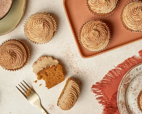  Pumpkin spice cupcakes with frosting, one cut in half, on a table