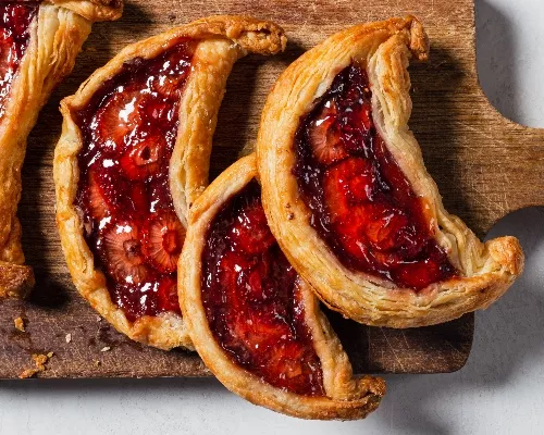 Four strawberry date galette crescents on a wooden cutting board