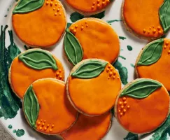 Shortbread cookies decorated to look like oranges on a white and green plate.