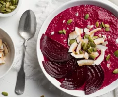 A bowl of red smoothie garnished with beet slices, seeds, and coconut