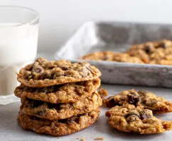 A stack of oatmeal chocolate chip cookies with a glass of milk and a tin serving tray.