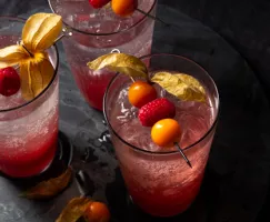 Three glasses of raspberry gooseberry shrub mixed with soda and garnished with raspberries and gooseberrries