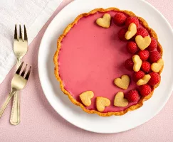 Raspberry rosewater panna cotta tart decorated with raspberries and heart-shaped cookies with 2 golden forks