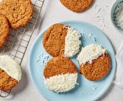 Gingersnap cookies half dipped in white chocolate and coconut on a blue plate and a wire cooling rack