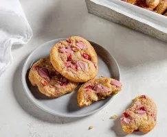Three strawberry and ruby chocolate chunk cookies on a plate, one broken in half